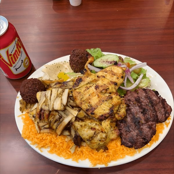 A large Mediterranean platter with grilled chicken, shawarma, falafel, rice, salad, and a soda.