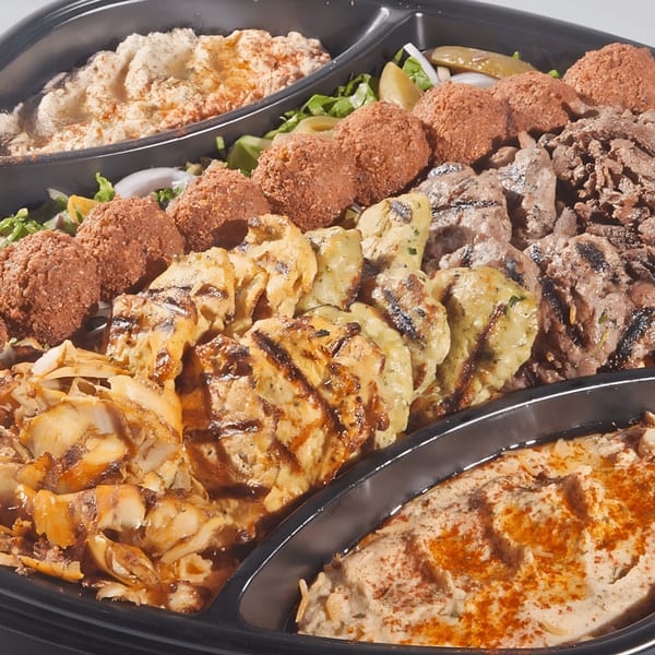 A large platter of Mediterranean food with hummus, falafel, grilled chicken, and beef shawarma.