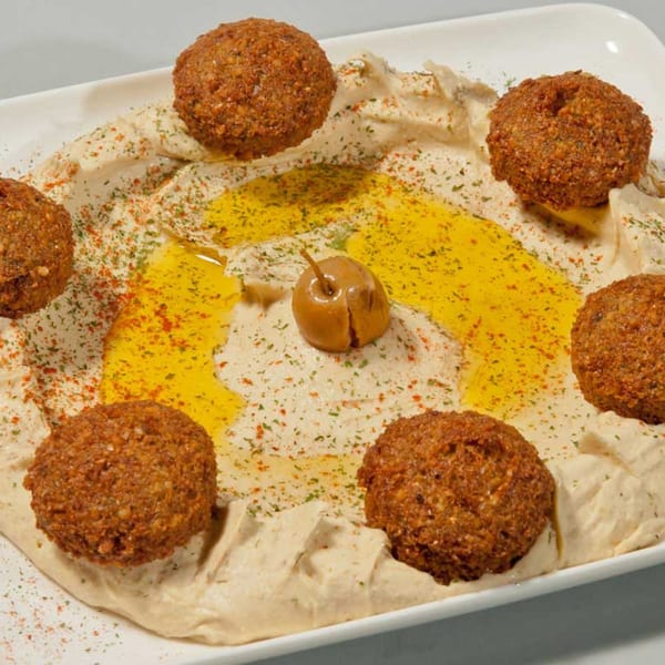 A white platter of hummus topped with falafel, olive oil, spices, and a single olive.