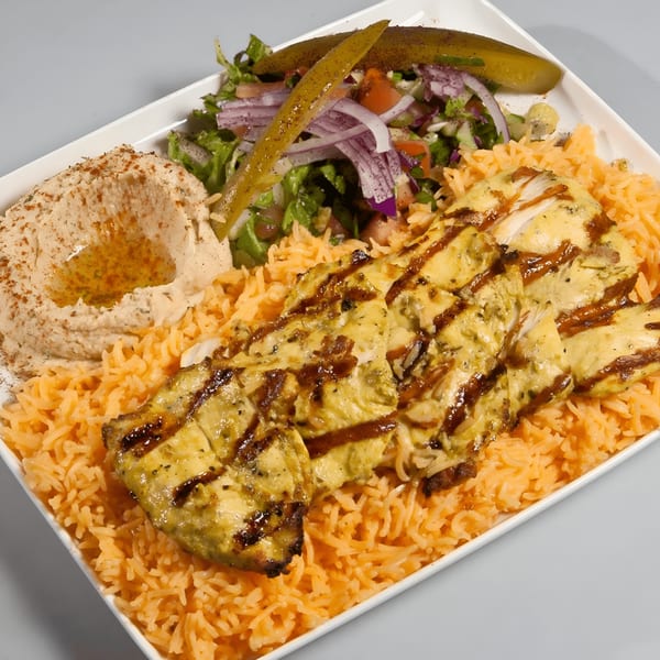 Grilled chicken with hummus, rice, salad, and pickles on a white rectangular plate.