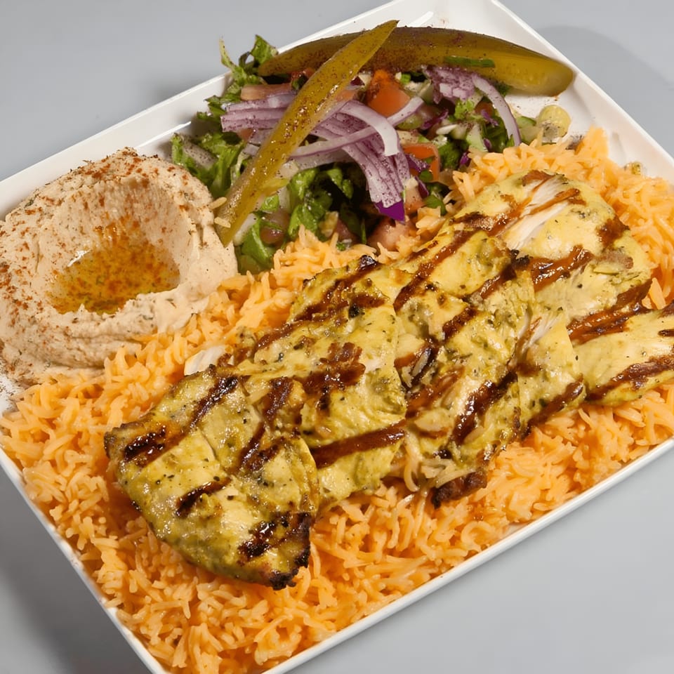 Grilled chicken with hummus, rice, salad, and pickles on a white rectangular plate.