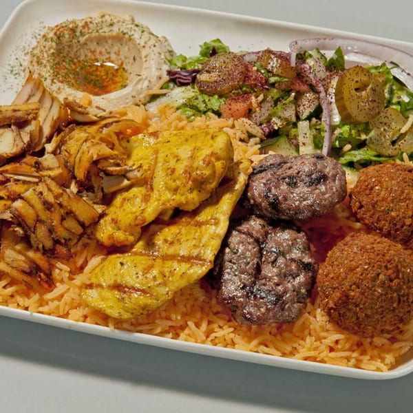 A large platter of Mediterranean food with chicken shawarma, grilled chicken, falafel, hummus, and salad.