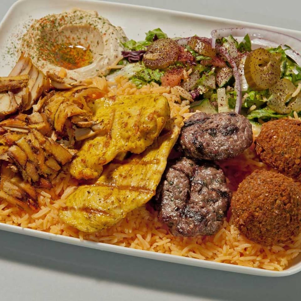A large platter of Mediterranean food with chicken shawarma, grilled chicken, falafel, hummus, and salad.